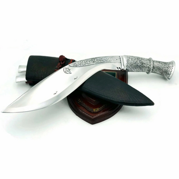 A 10 inch hand forged kukri with a polished blade and a brass handle, accompanied by a black leather scabbard, displayed on a wooden surface.